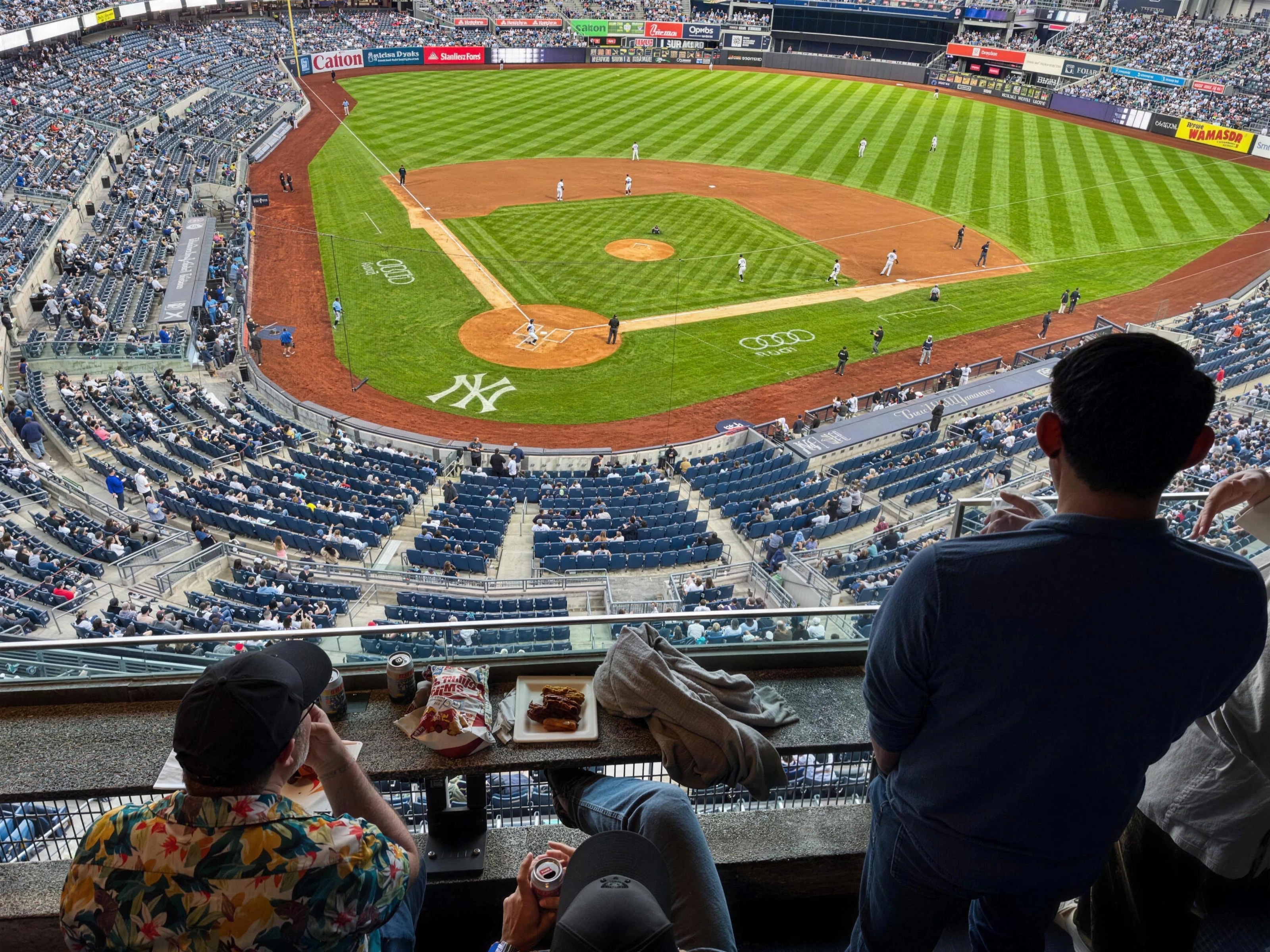 Guests watching a baseball game from a stadium suite, the field and infield spread out below them.